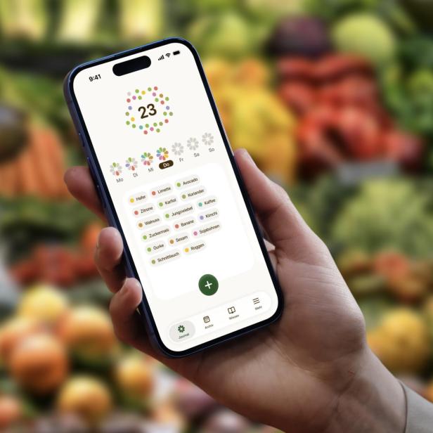 Hand hält Smartphone mit geöffneter Ernährungs-App vor unscharfem Gemüse-Hintergrund.