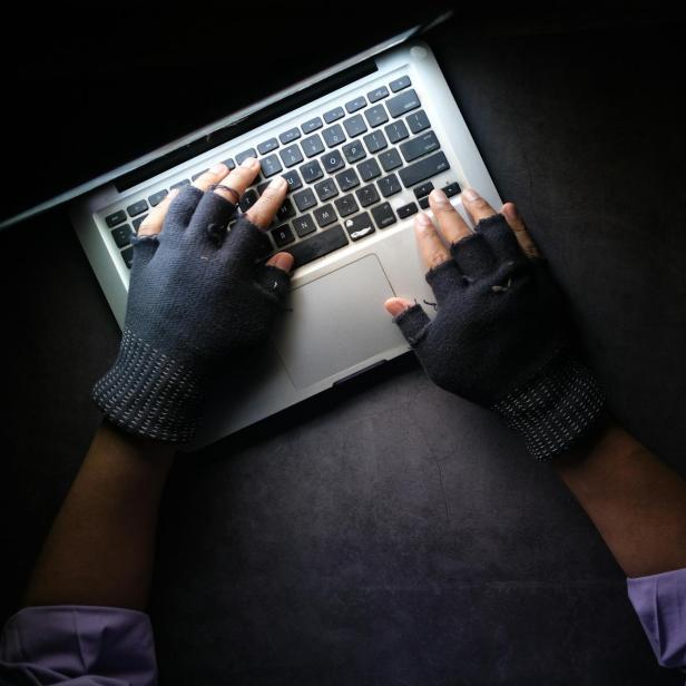 Person mit fingerlosen Handschuhen tippt auf einer Laptop-Tastatur im Dunkeln.