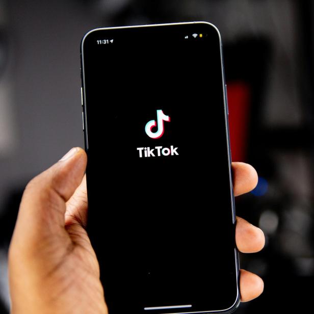 Hand hält Smartphone mit geöffnetem TikTok-Startbildschirm.