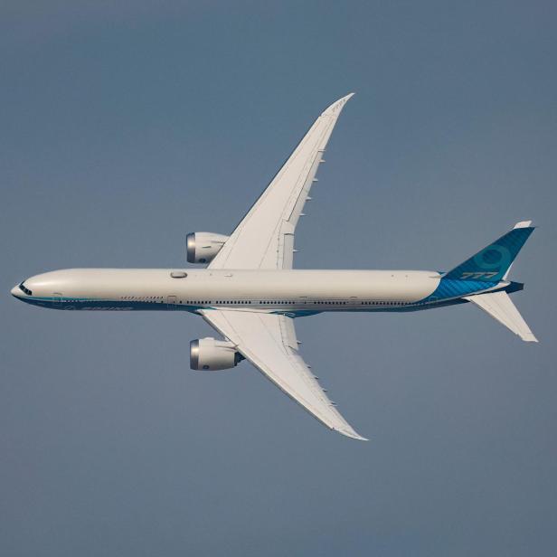 Ein weißes Boeing 777 Flugzeug fliegt am blauen Himmel.