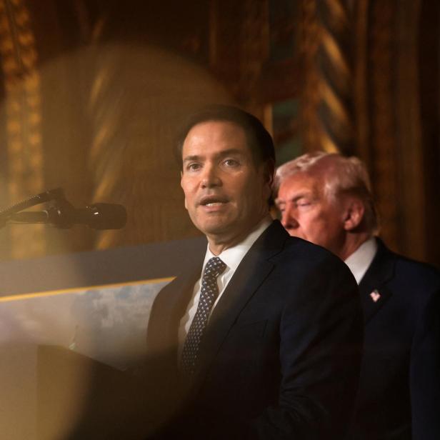 Marco Rubio spricht am Rednerpult, während Donald Trump im Hintergrund steht.