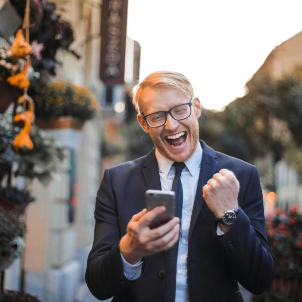 Mann im Anzug freut sich draußen über eine Nachricht auf seinem Smartphone.