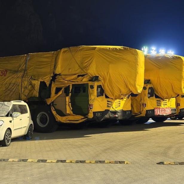Mehrere Lkw mit gelben Planen und Zoomlion-Beschriftung stehen nachts auf einem Parkplatz.