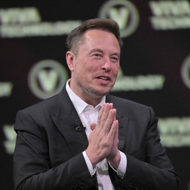 Elon Musk im Anzug hält die Hände zusammen.