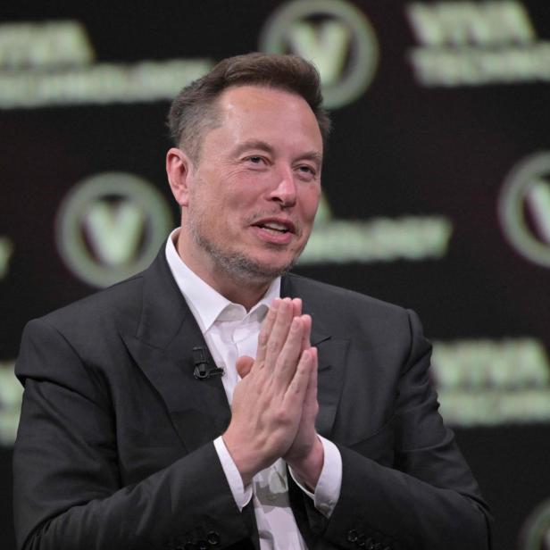 Elon Musk im Anzug hält die Hände zusammen.