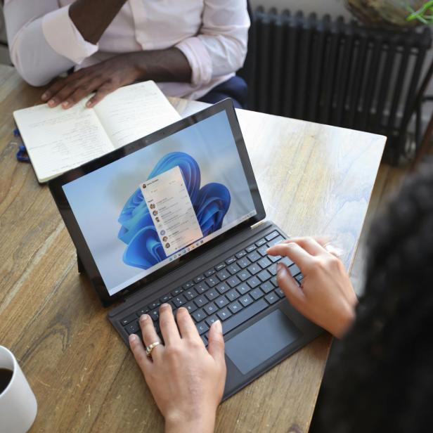 Zwei Personen sitzen am Tisch und arbeiten. Eine Person mit einem Laptop