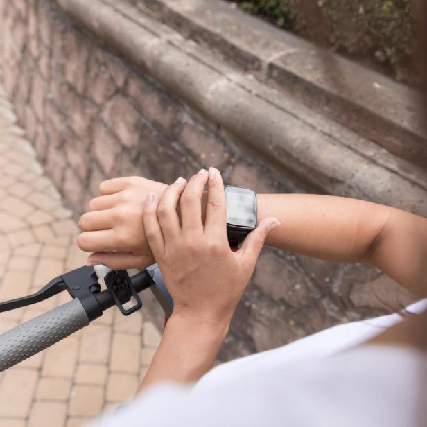 Eine Frau hält den Lenker ihres Fahrrads und drückt einen Knopf auf ihrer Smartwatch.