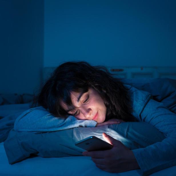 Eine Frau mit Handy im Bett.