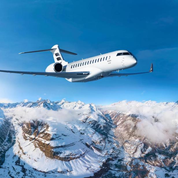 Bombardier Global 8000 fliegt über verschneite Alpen mit klarem Himmel im Hintergrund.