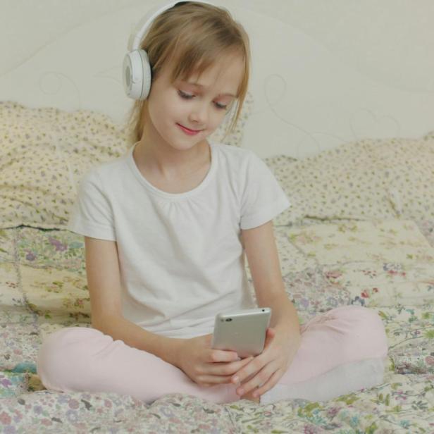 Ein Mädchen sitzt mit ihrem Smartphone am Bett 