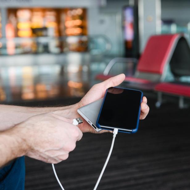 Eine Person hält ein Smartphone und eine Powerbank in der Hand und verbindet sie mit einem Ladekabel.