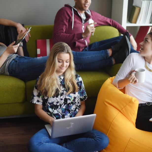Eine Gruppe junger Leute entspannt mit Laptops, Tablets und Getränken auf einem grünen Sofa und einem gelben Sitzsack.