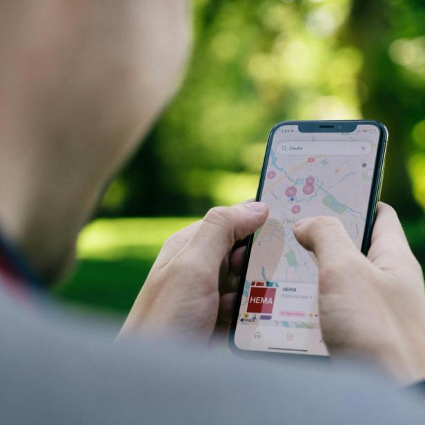 Person hält Handy in der Hand, auf dem Google Maps geöffnet ist, Hintergrund ist ein Park