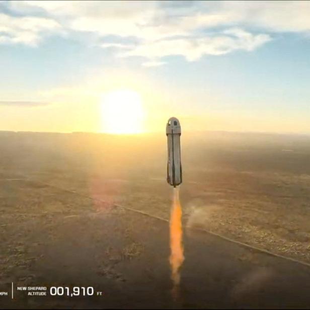 Eine Rakete steigt bei Sonnenaufgang mit orangefarbenem Abgasstrahl über eine weite Landschaft auf.