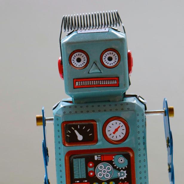 Blechspielzeug-Roboter mit aufgemalten Anzeigen und Spiralfeder auf dem Kopf vor grauem Hintergrund.