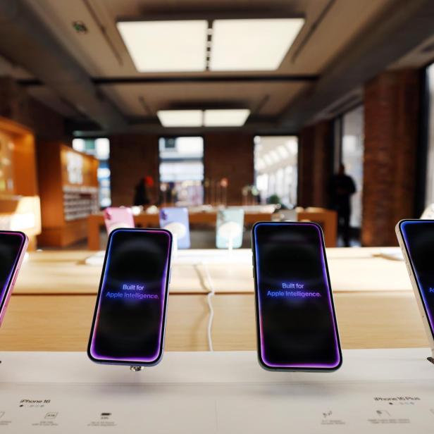 Vier moderne Smartphones mit leuchtenden Displays stehen nebeneinander auf einem Verkaufstisch in einem hellen Geschäft.
