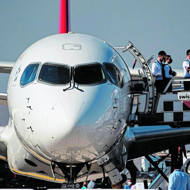 Ein Flugzeug steht am Boden, während mehrere Crewmitglieder an einer geöffneten Tür auf einer Fluggastbrücke stehen.