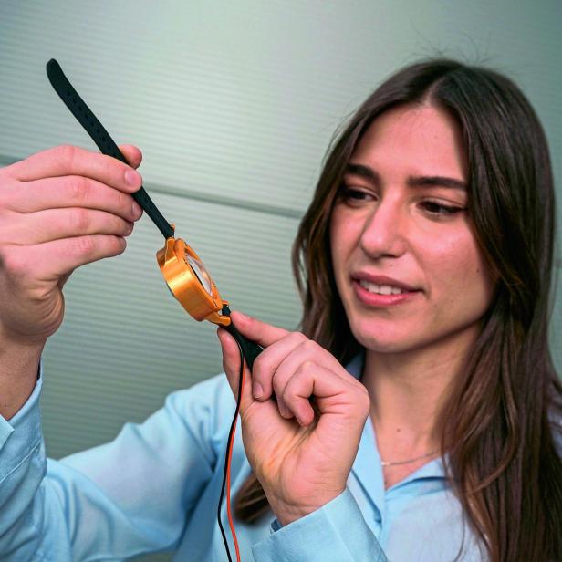 Eine Frau hält eine orangefarbene Armbanduhr mit schwarzem Armband und betrachtet sie aufmerksam.