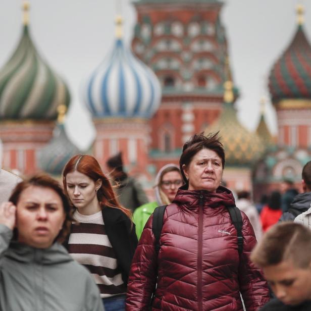 Mehrere Menschen gehen vor den bunten Zwiebeltürmen der Basilius-Kathedrale in Moskau entlang.