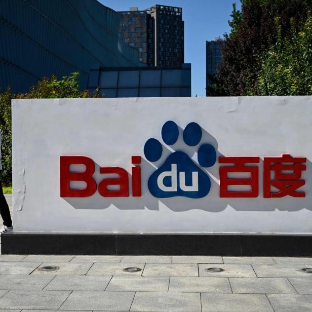 Ein Mann mit Maske geht an einem großen Baidu-Logo mit Pfotenabdruck im Freien vorbei.