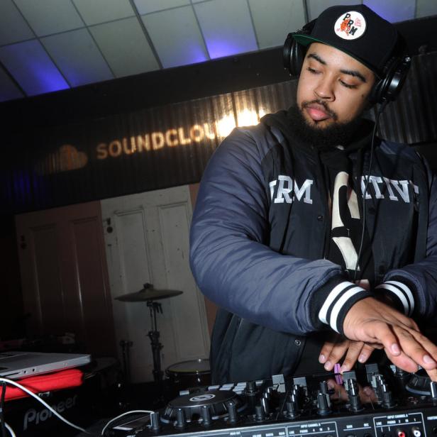 Ein DJ mit Kopfhörern legt in einem Club vor einem „SoundCloud“-Schriftzug auf.