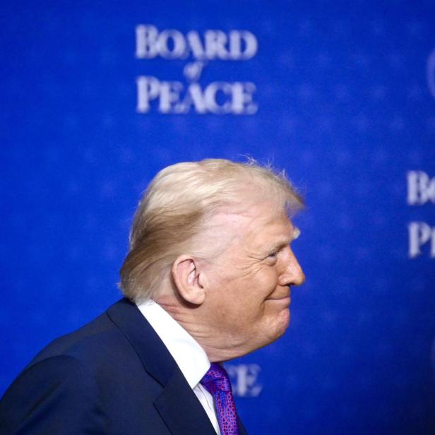 Ein Mann im Anzug mit blonden Haaren steht seitlich vor blauem Hintergrund mit der Aufschrift „Board of Peace“.