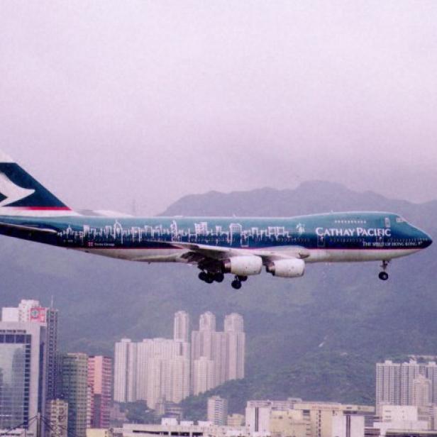 Flugzeug von Cathay Pacific im Landeanflug über Hochhäusern vor Bergen in Hongkong.