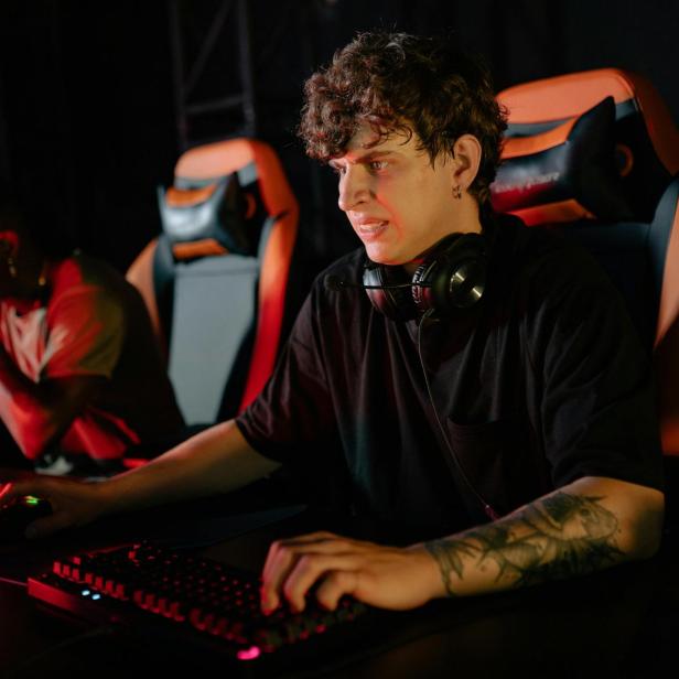 Zwei junge Männer sitzen an Gaming-PCs, einer wirkt frustriert, der andere konzentriert.