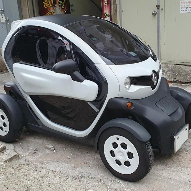 Ein weiß-schwarzer Renault Twizy steht auf einer leicht beschädigten Straße vor einem Gebäude.