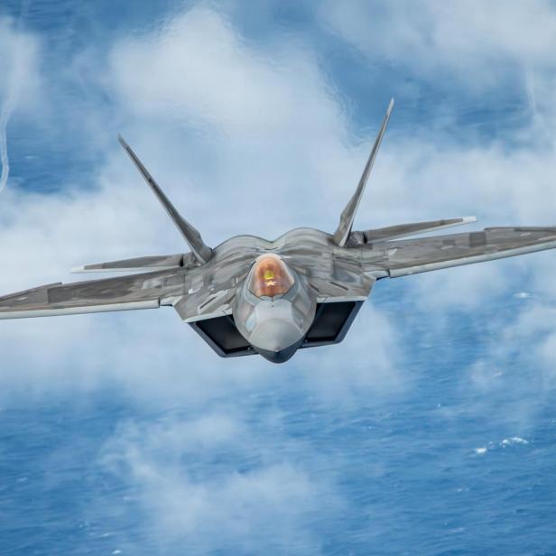 Ein F-22-Kampfjet fliegt über Wolken und Ozean in Richtung Kamera.