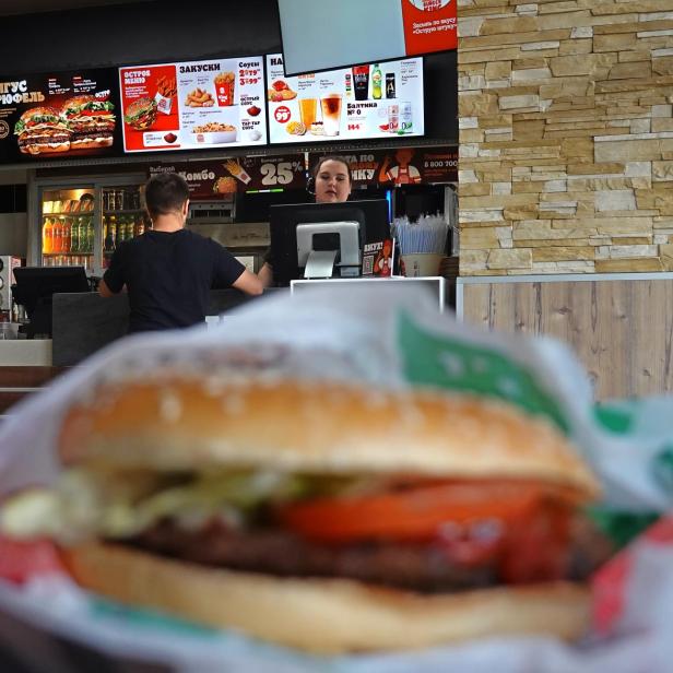 In einem Burger King Restaurant stehen ein Burger, ein Getränk und Kunden vor der Theke.