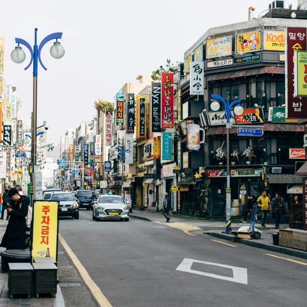 Belebte Straße in Südkorea mit zahlreichen Geschäften und bunten Schildern auf Koreanisch.