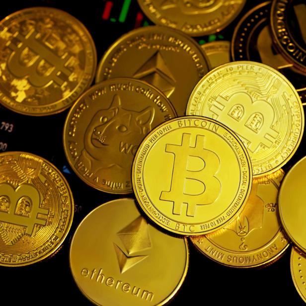 Goldene Münzen mit Symbolen von Bitcoin, Ethereum und Dogecoin auf schwarzem Hintergrund.