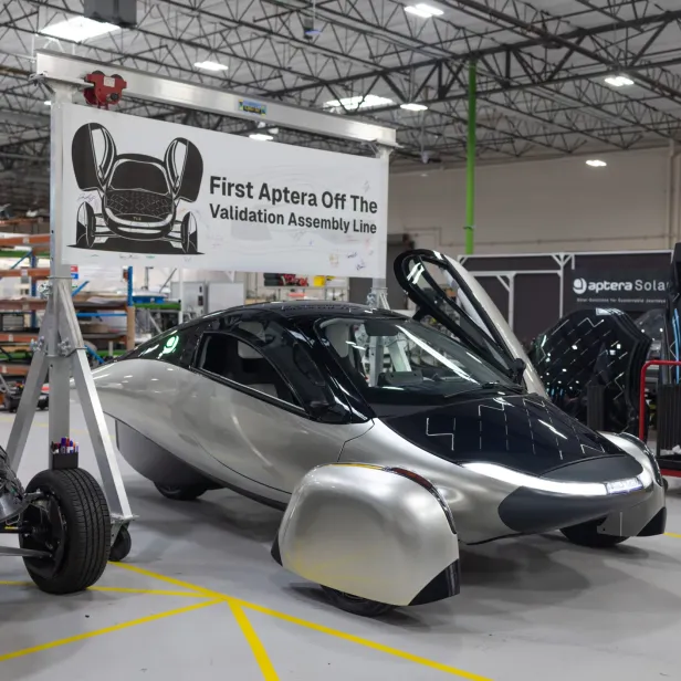 Das erste fertige Aptera-Solarauto steht mit geöffneten Türen in einer Fabrikhalle.