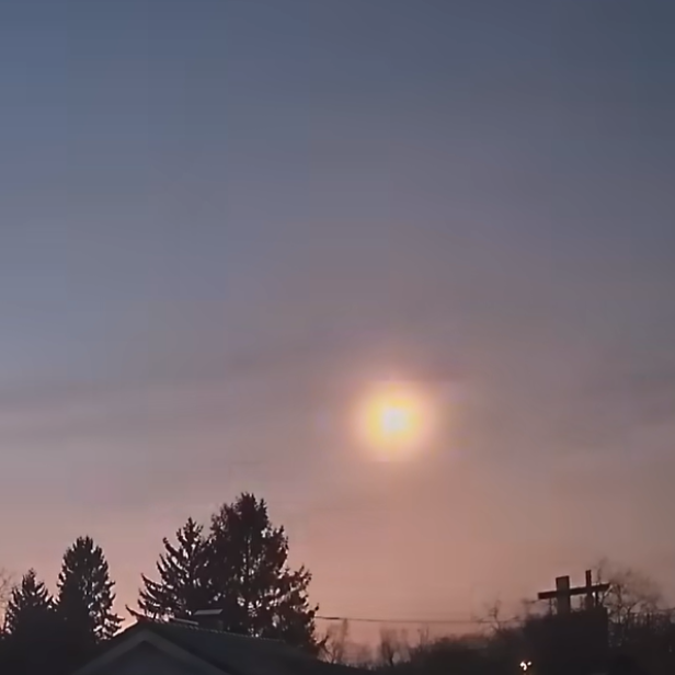 Leuchtender Meteor am Abendhimmel über einer Häuser- und Baumreihe.