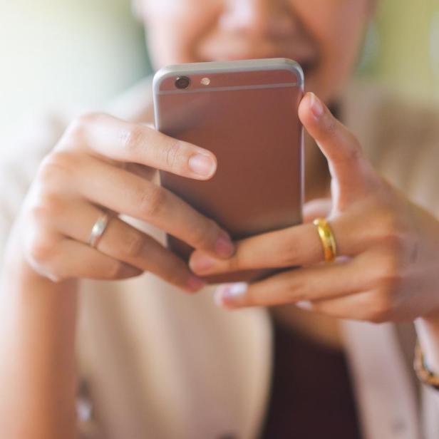Eine Person hält ein Smartphone mit beiden Händen vor sich. (Symbolbild)