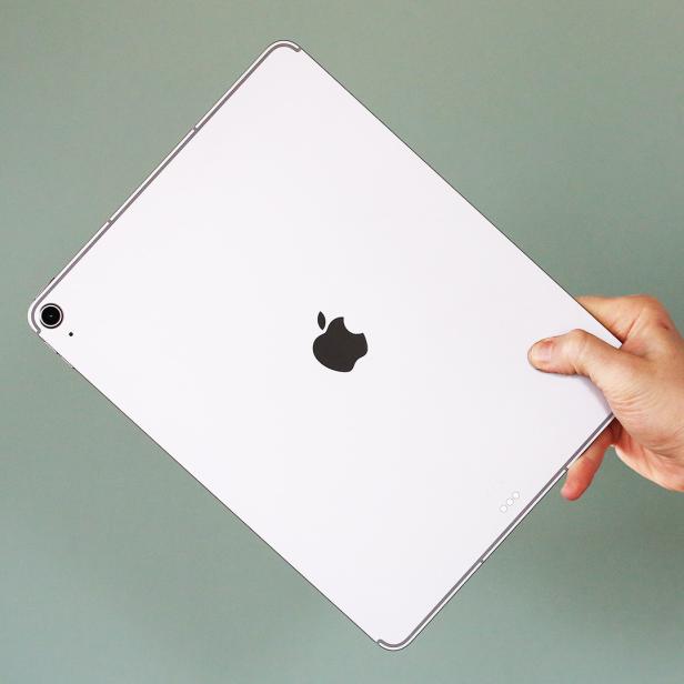 Eine Hand hält ein silbernes iPad Air 13 vor grünem Hintergrund.