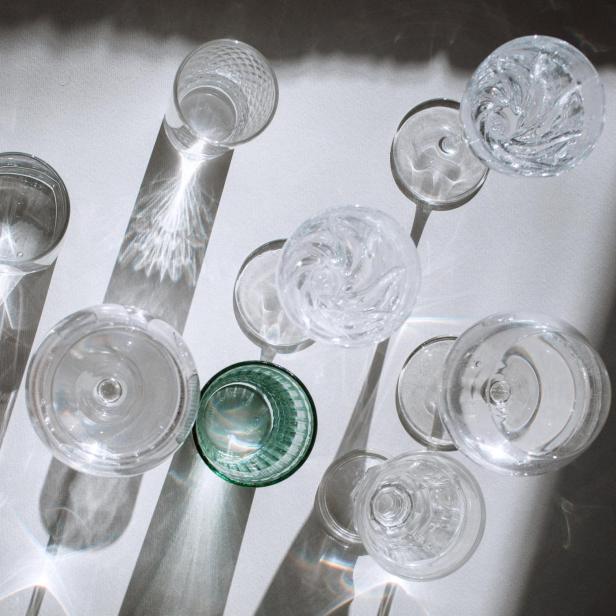 Mehrere leere Glasgefäße werfen Lichtreflexe und Schatten auf eine helle Oberfläche.