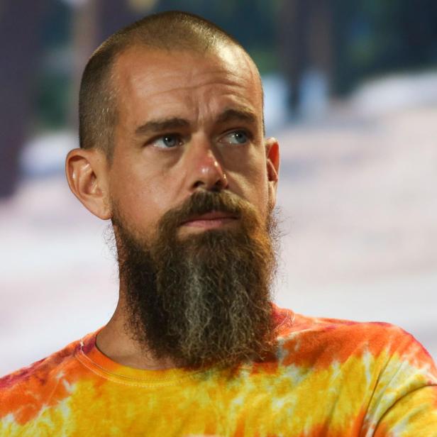 Ein Mann mit Vollbart und Glatze trägt ein buntes Batik-T-Shirt und blickt nachdenklich zur Seite.