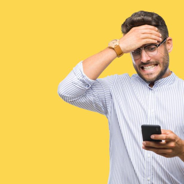 Ein Mann mit Brille und Hemd blickt entsetzt auf sein Handy vor gelbem Hintergrund.