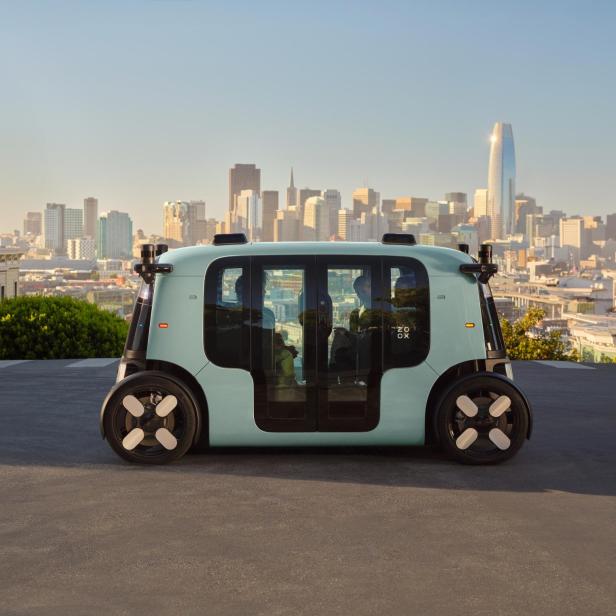 Autonomes Zoox-Robotaxi vor Skyline einer US-Großstadt bei Tageslicht.