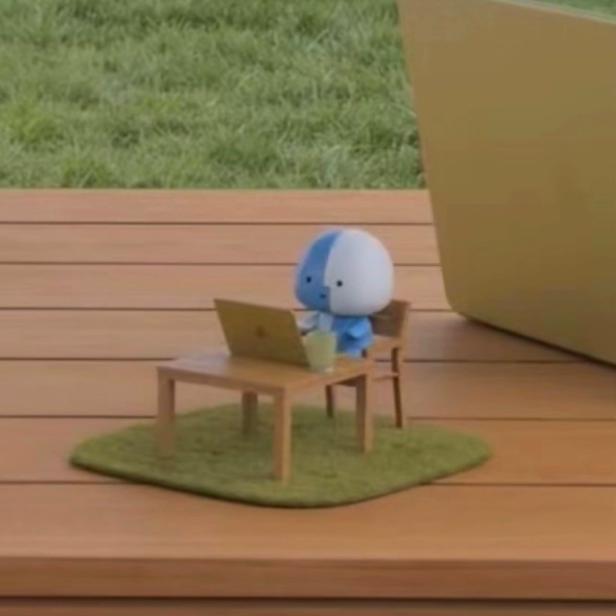 Apple-Maskottchen Lil Finder Guy sitzt auf einem Mini-Schreibtisch auf einem richtigen Tisch
