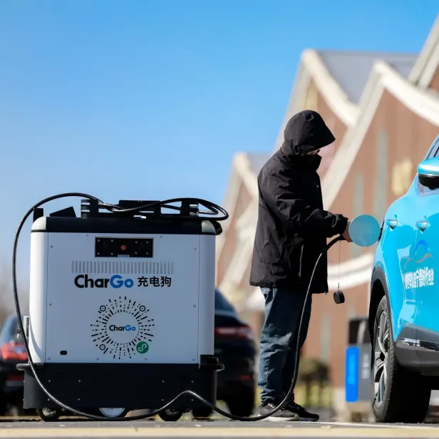 Eine Person lädt ein blaues Elektroauto mit einem mobilen Lade-Roboter namens CharGo auf.