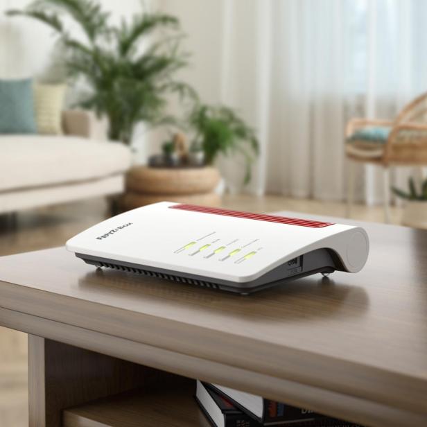 Ein WLAN-Router mit leuchtenden Anzeigen steht auf einem Holztisch in einem gemütlich eingerichteten Wohnzimmer.