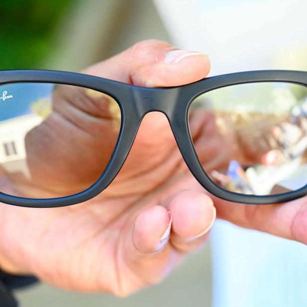 Eine Hand hält eine schwarze Ray-Ban-Brille mit integrierten Kameras an den Ecken des Rahmens.