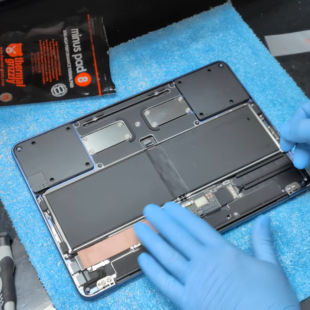 Geöffnetes MacBook Neo mit sichtbarem Innenleben und blauen Handschuhen bei der Montage.