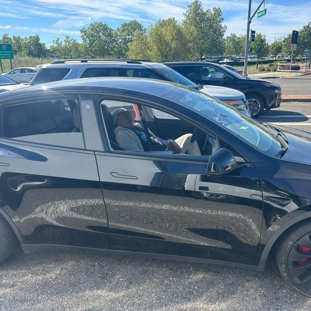 Eine Person schläft am Steuer eines schwarzen Tesla an einer belebten Straßenkreuzung.