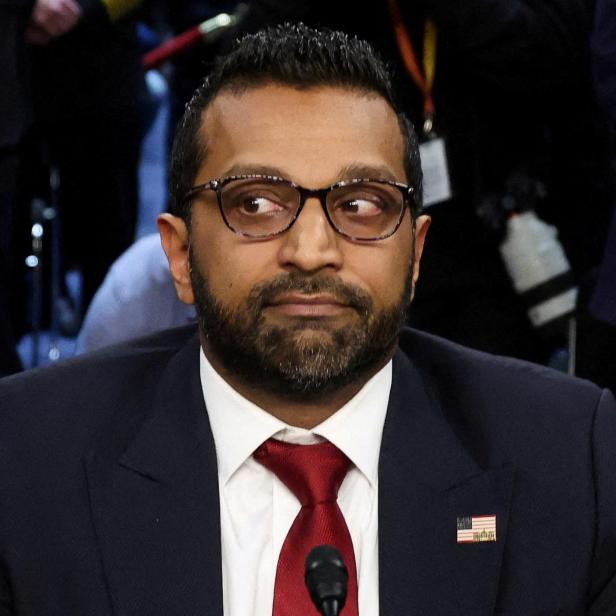 Ein Mann mit Brille und roter Krawatte sitzt im Anzug an einem Tisch und blickt zur Seite.