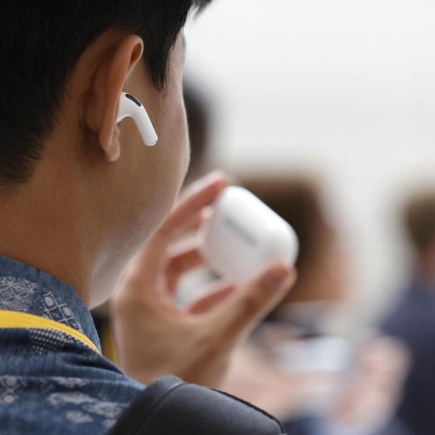 Eine Person hält AirPods-Kopfhörer und ein iPhone in der Hand