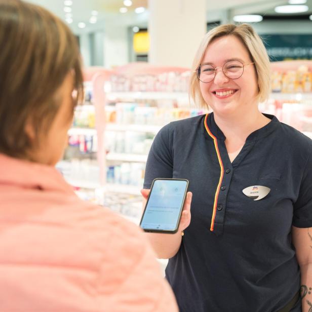 dm-Mitarbeiterin mit Smartphone in der Hand in Filiale mit Kundin